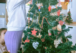 Dziewczynka zakłada gwiazdę na czubek choinki