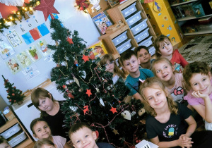 Dzieci siedzą wokół ubranej choinki