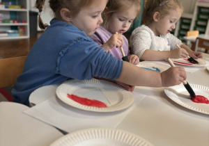 Dziewczynka maluje talerzyk na czerwono