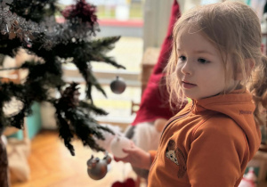 Dziewcyznka zakłada białą bombkę na choinkę