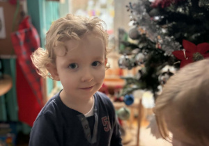 Chłopiec stoi na tle choinki