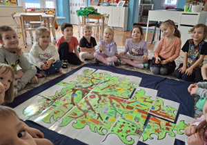 Grupa dzieci siedzi przed choinką z puzzli