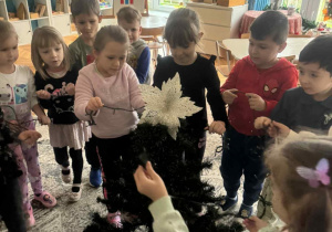 Dzieci zakładają lampki na choinkę