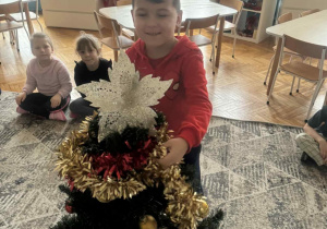 Chlopiec zakłada gwiazdę na czubek choinki