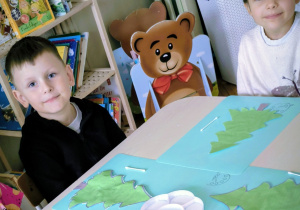 Dzieci siedzą przy stole z wyciętym szablonem choinki