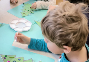 Chłopiec przykleja cekiny na szablon zielonej choinki