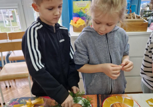 Chłopiec dokleja gałązki na talerzyk papierowy