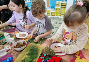 Dzieci obklejaja talerzyk zielonymi gałązkami