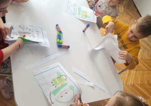 Dzieci przy stoliku wycinają puzzle z bałwanami