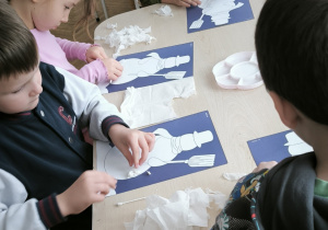 Dzieci siedzą przy stolikach i naklejają bałwany