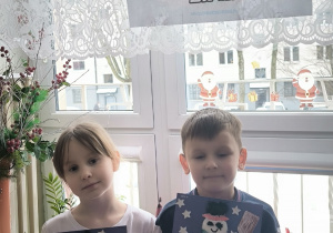 Chłopiec z dziewczynką stoją pod napisem zima z pracą plastyczna z bałwankiem