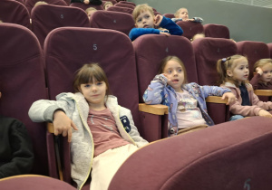 Dzieci siedzą na czerwonych krzesłach