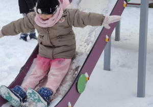 Dziewczynka bez trzymanki zjeżdża po zjeżdżalni