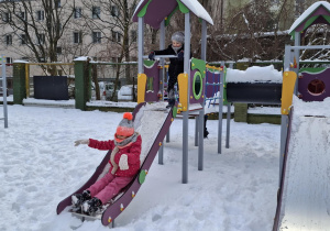 Dziewczynka w czerwonym kombinezonie zjezdża ze zjeżdżalni