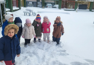 dzieci stoją w śniegu w ogrodzie