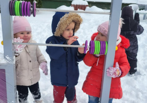 troje dzieci bawi się sprzętem z ogrodu przedszkolnego