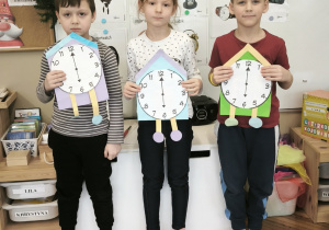 Dwóch chłopców i dziewczynka stoją z zegarami