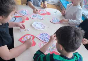 Dzieci przy stole naklejają na serduszka kolorowe kartki