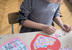 Dziewczynka wykleja kolorowymi kartkami środek serca