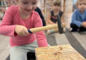 Dziewczynka wbija gwóźdź w deskę