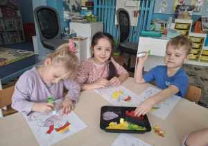 Dziewczynka wykleja kurtkę chłopca kolorowym papierem