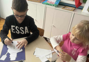 Chłopiec nakelja bałwana na niebieski karton