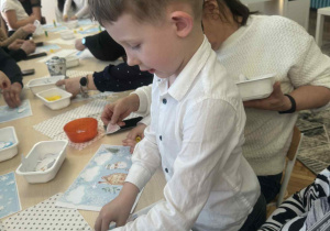 Chłopiec przykleja domek na zimowy obrazek