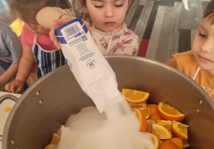 Dziewczynka wsypuje cukier do dużego garnka z owocami