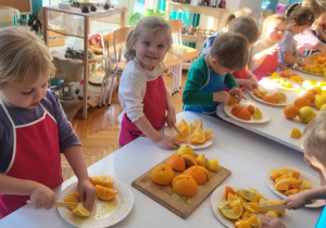 dzieci stojąw fartuszkach i kroją owoce