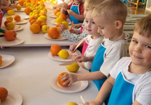 dzieci stojąw fartuszkach i kroją owoce