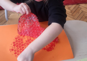 dziecko wykonuje pracę plastyczną, odkleja serce z folii bąbelkowej pozostawiając wzór serca na kartonie