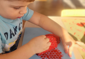 dziecko wykonuje pracę plastyczną, odkleja serce z folii bąbelkowej pozostawiając wzór serca na kartonie