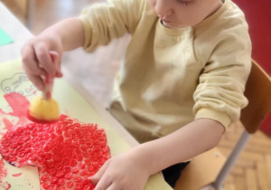 dziecko wykonuje pracę plastyczną, odkleja serce z folii bąbelkowej pozostawiając wzór serca na kartonie