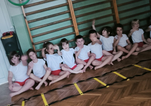 Dzieci siedzą na sali gimnastycznej w strojach