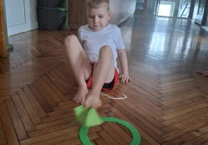 Chłopiec palcami stóp podnosi woreczek do góry