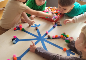 dzieci siedzą przy stoliku i układdają kulki w kształcie śnieżynki