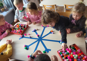 dzieci siedzą przy stoliku i układdają kulki w kształcie śnieżynki