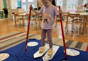 Dziewczynka stoi ubrana w narty z kijkami