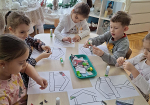 Dzieci przy stoliku wyklejają gazetami karmnik