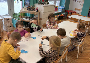 Dzieci przy siedzą przy stole z papierowymi łyżwami