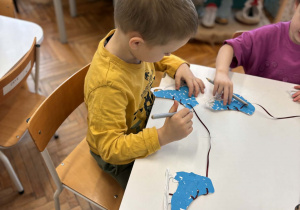 Chłopiec przeciąga tasiemkę przez dziurki łyżew