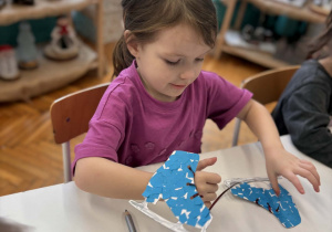 Dziewczynka przeciąga tasiemkę przez otwory na sznurowadła