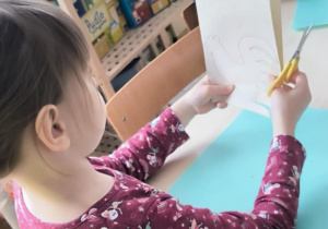 Dziewczynka składa papier na pół z naryzowanym kogucikiem