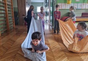 Chłopiec siedzi na pościeli a dziewczynki go ciągną