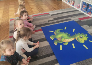 ieci siedza na dywanie przed dużym ibrazkiem dinozaura