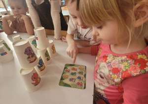 Dziewczynka układa kubeczki z dinozaurami według wzoru