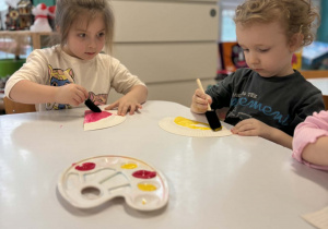 Dzieci malują talerzyki na różowo i żółto