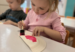 Dziewczynka maluje talerzyk na różowo