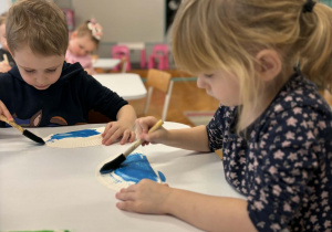 Dziewczynka z chłopcem maluje talerzyk na niebiesko