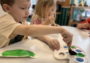 Chłopiec macza pędzel w zielonej farbie